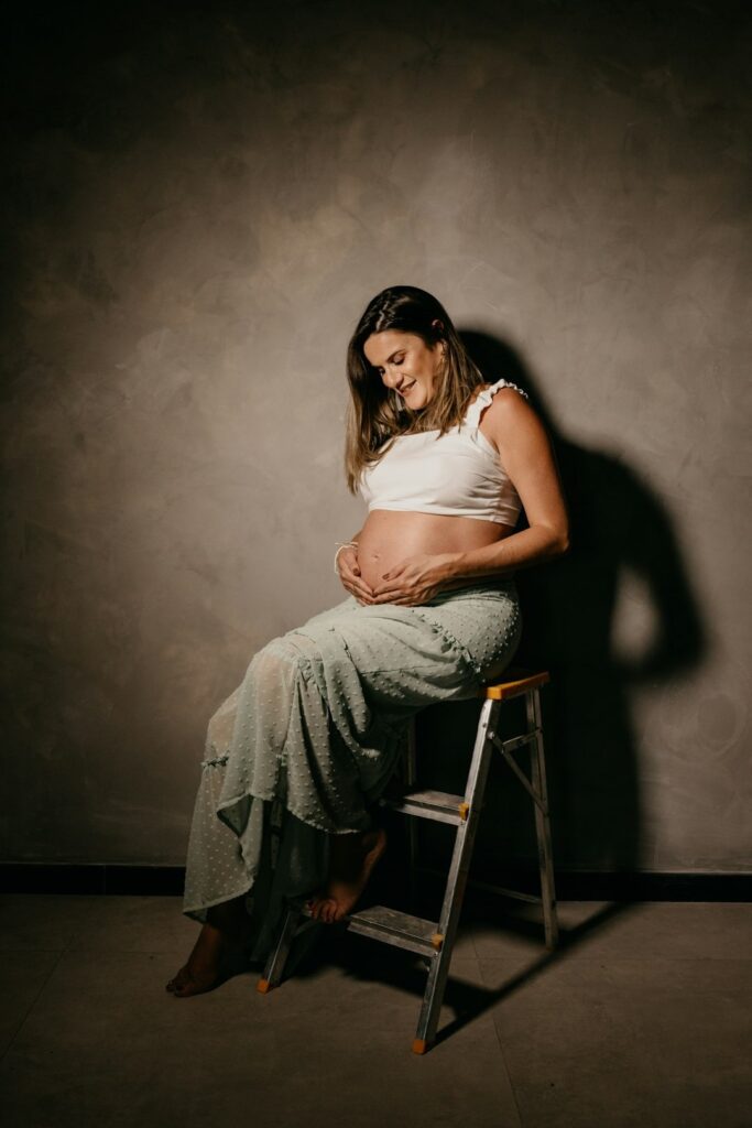 Pregnant woman smiling while resting on a metal stepladder.
