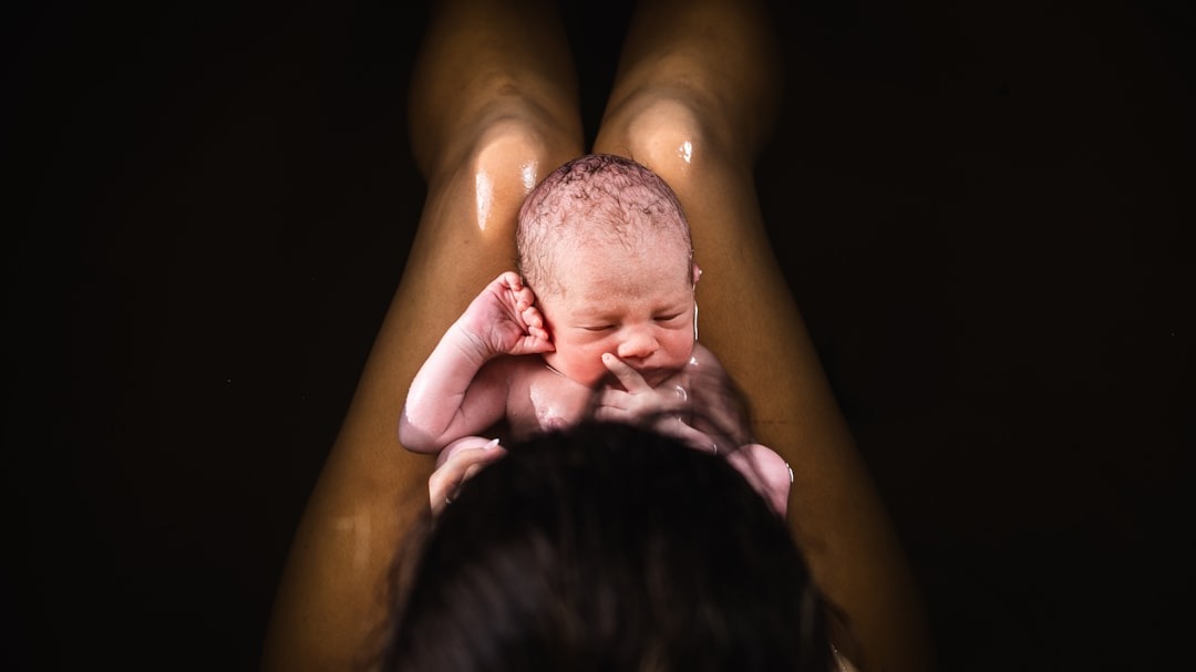 A newborn baby rests in water held by a parent.
