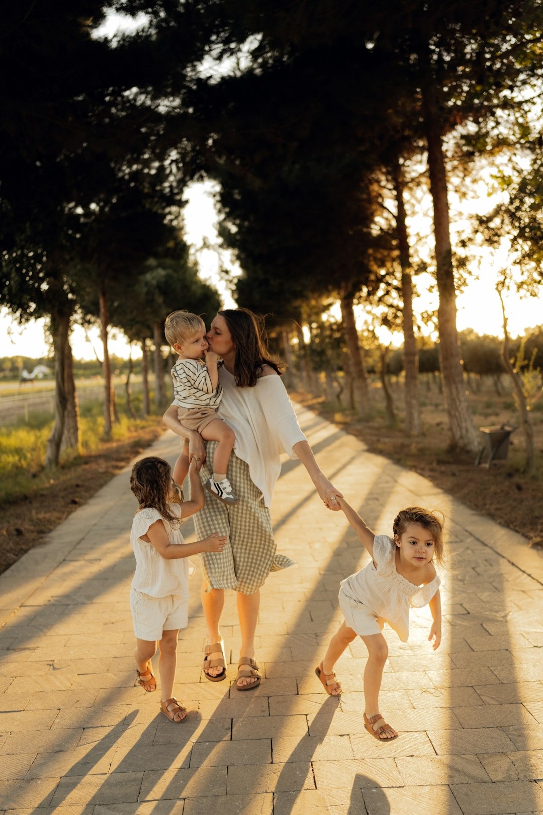 Mother carries her son and holds hands with daughters walking outdoors.